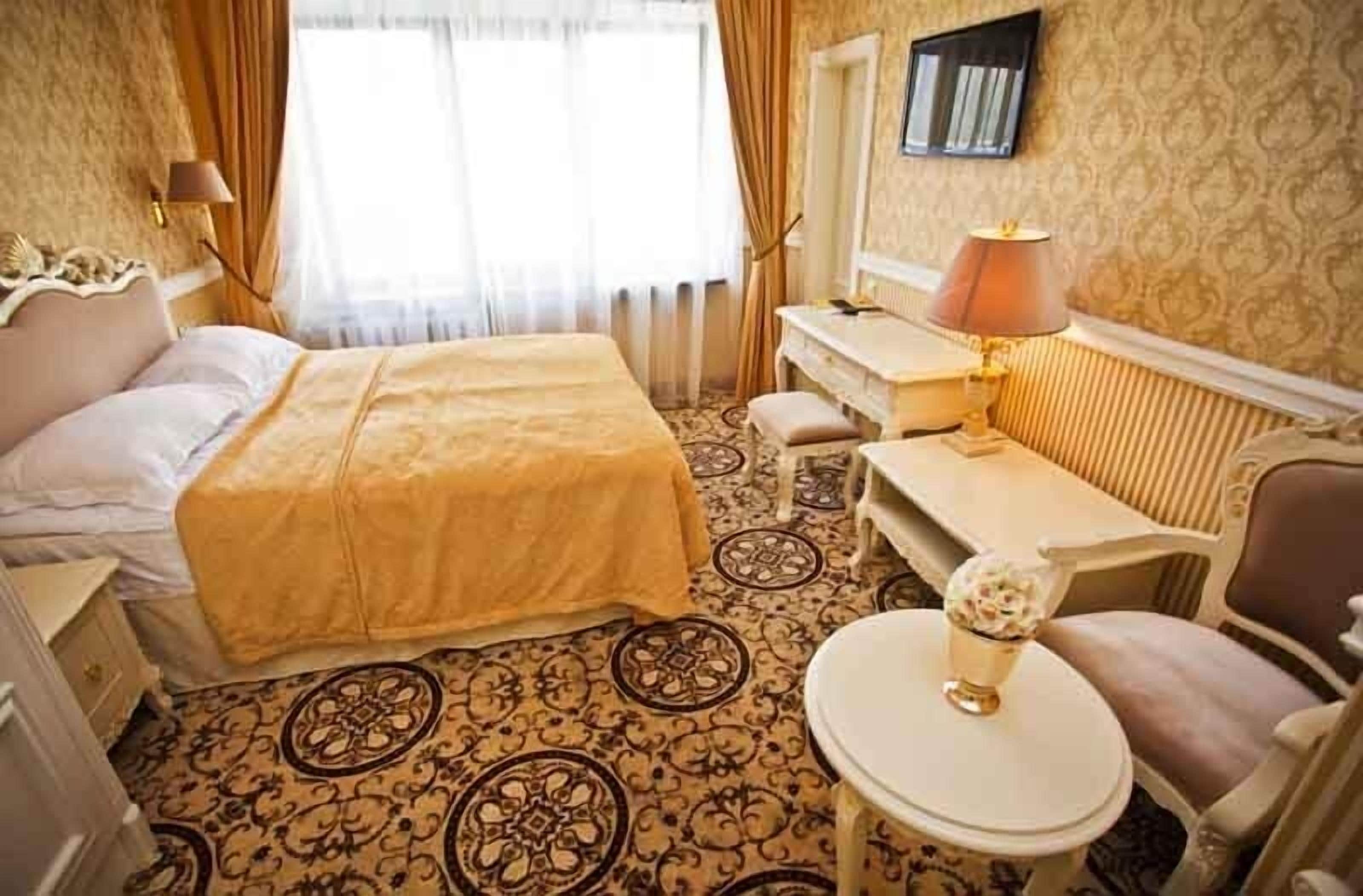 Une chambre d’hôtel avec un lit, un bureau, une chaise, une petite table avec une lampe et un téléviseur fixé au mur.