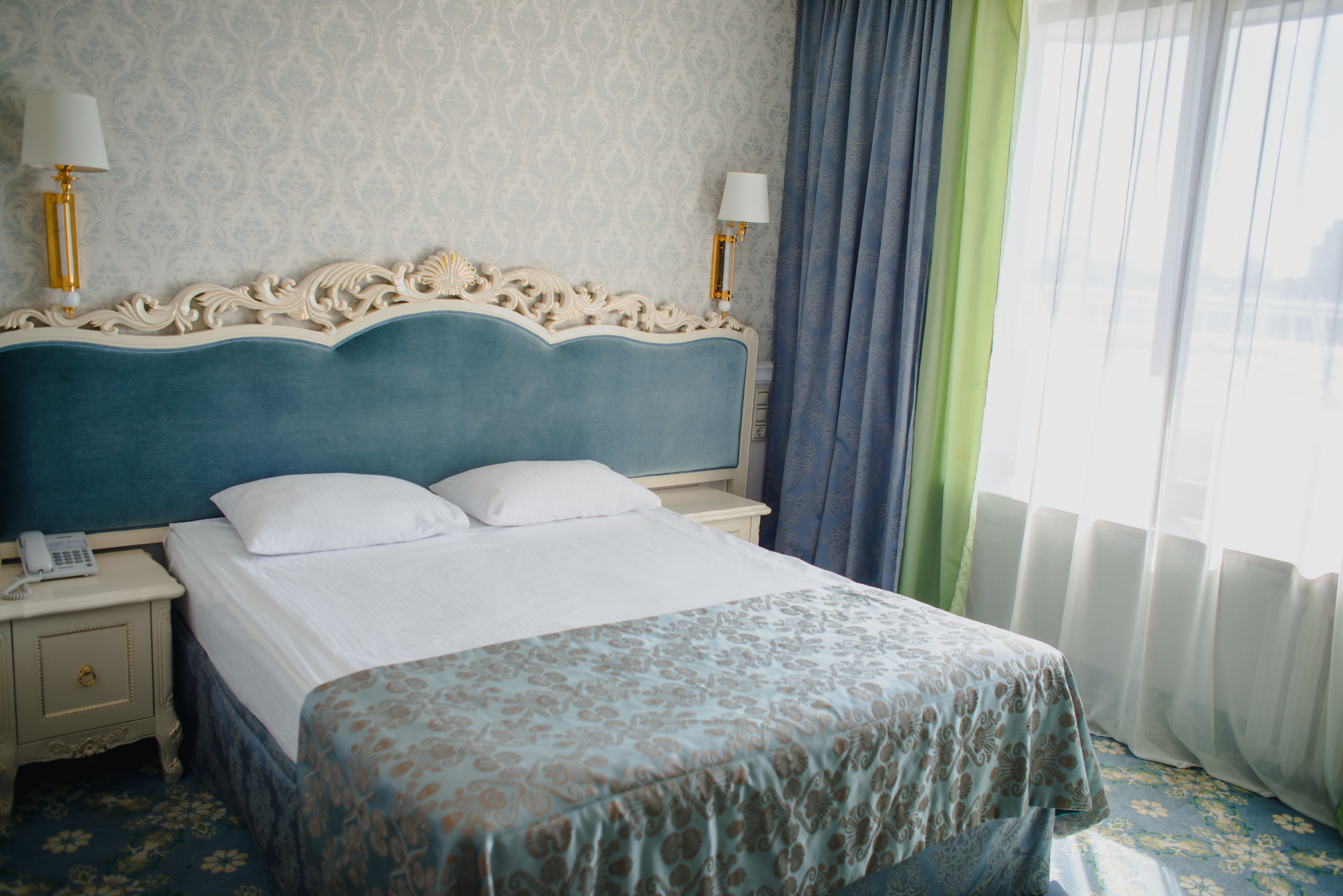 A hotel room with a large bed, two bedside tables, a lamp, and a window with curtains.