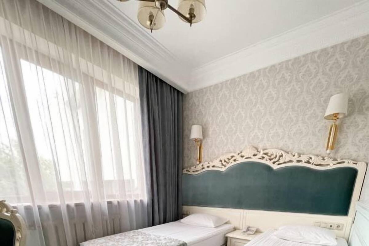 Een hotelkamer met twee enkele bedden, een nachtkastje, een stoel en een raam met gordijnen.