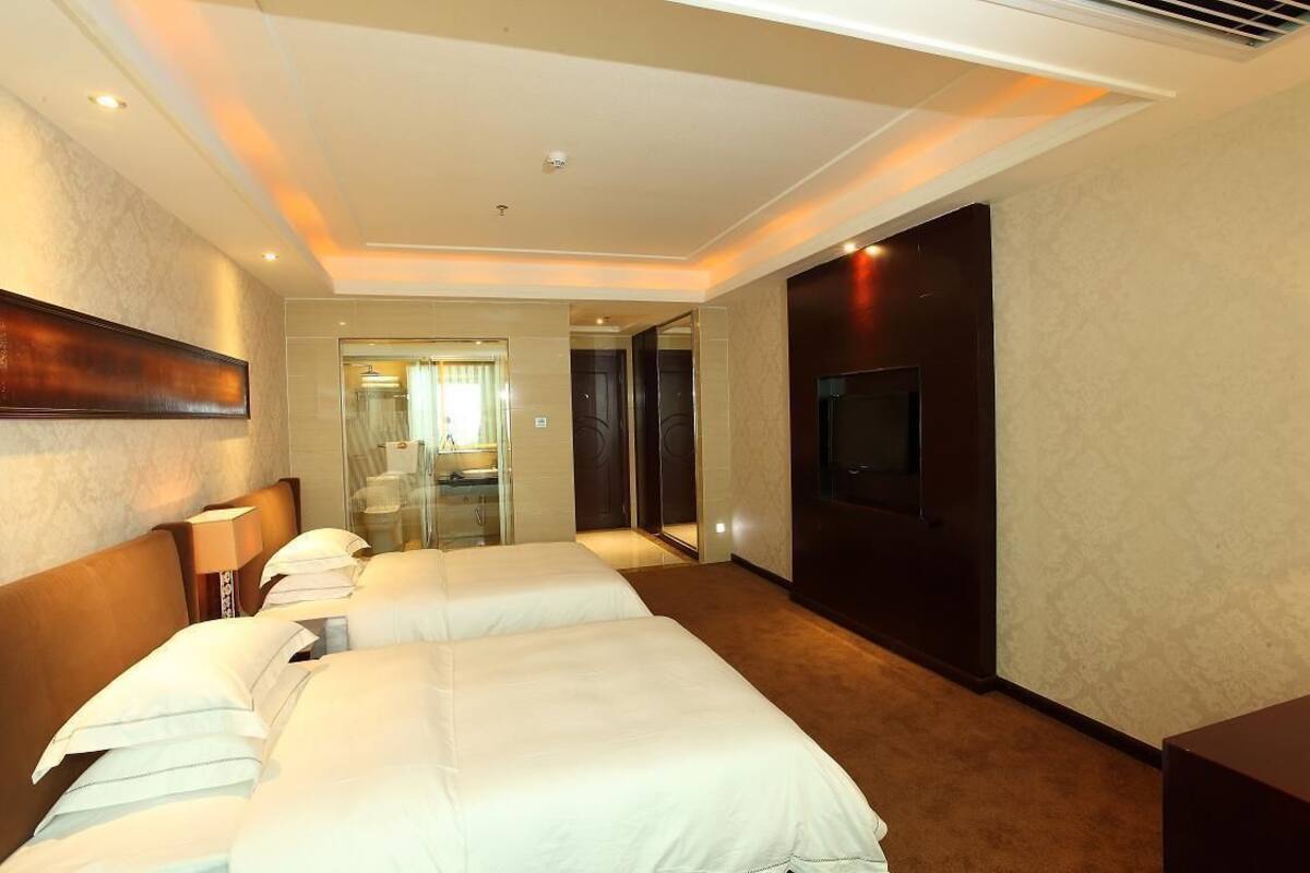 Habitación de hotel con dos camas, un televisor y un baño visible a través de una puerta de cristal.