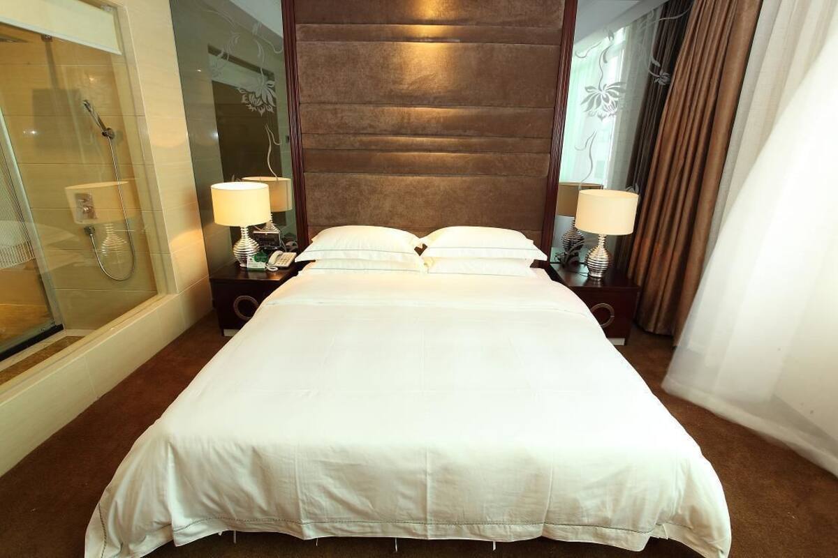 Una habitación de hotel con una cama grande, dos lámparas de noche, ducha y zona de ducha con paredes de vidrio.