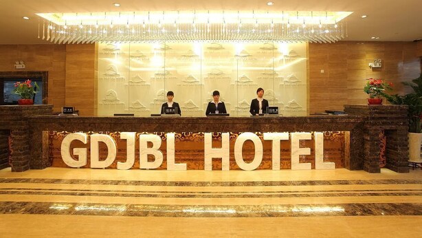 A reception desk at the GDJBL Hotel with three staff members seated behind it. - Guangdong Jin Bao Lai Hotel (Guangzhou)
