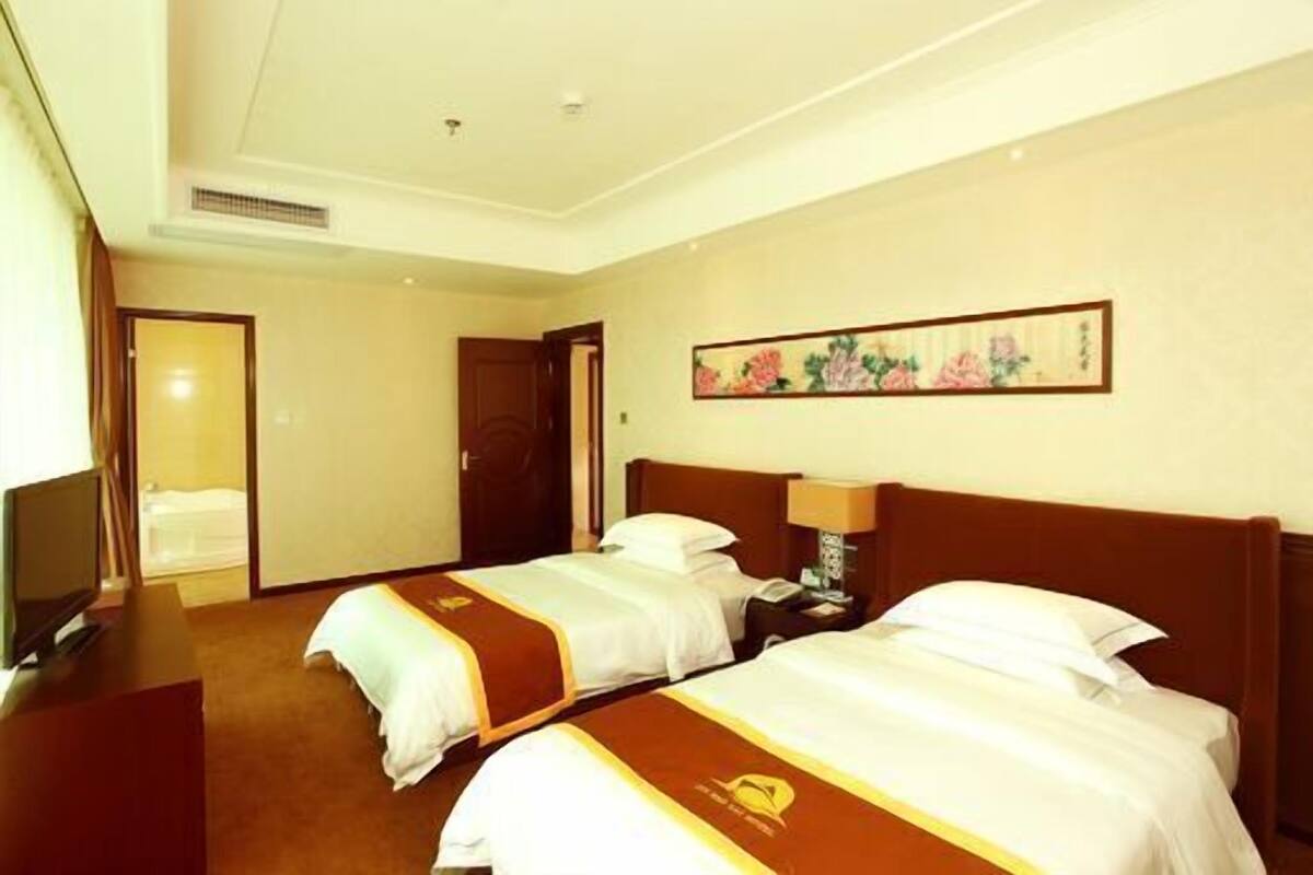 Habitación de hotel con dos camas, un televisor y un cuadro en la pared.
