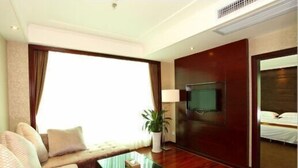 A hotel room with a sofa, a glass coffee table, a TV, and a bed. - Guangdong Jin Bao Lai Hotel (Guangzhou)