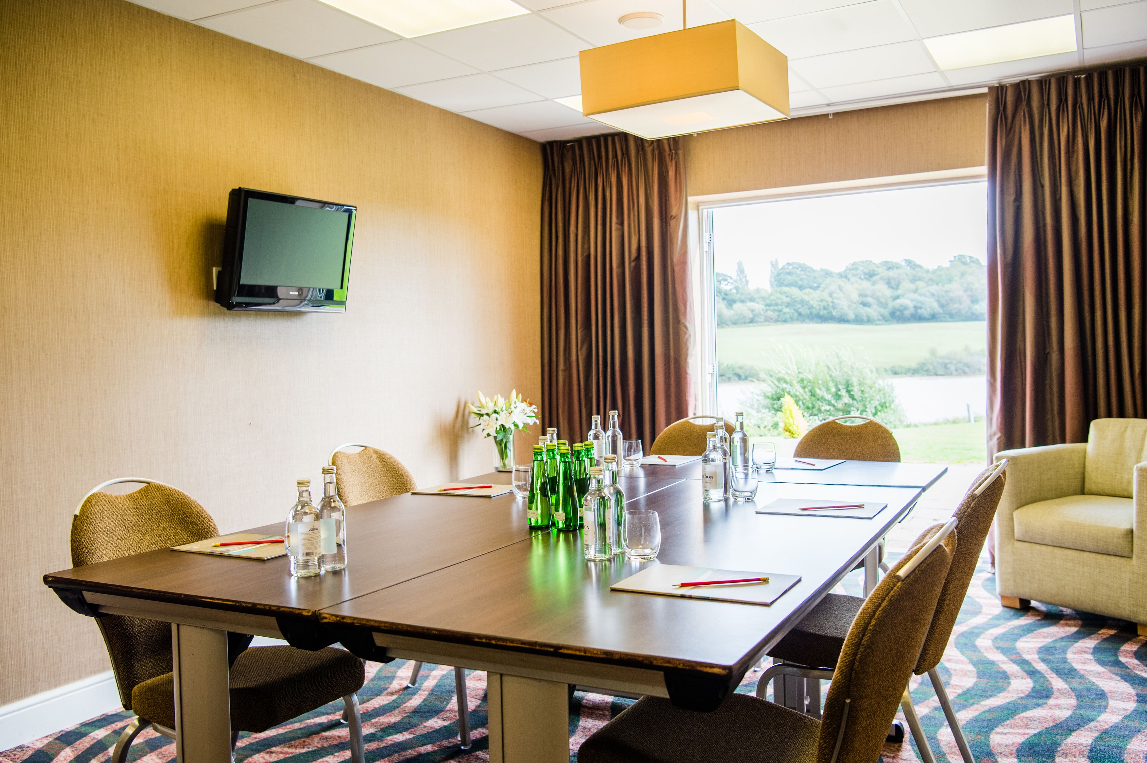 Ein Konferenzraum mit langem Tisch, Stühlen, einem Fernseher an der Wand und Blick ins Freie durch große Fenster.