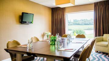 Ein Konferenzraum mit langem Tisch, Stühlen, einem Fernseher an der Wand und Blick ins Freie durch große Fenster.