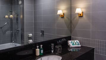 Un baño moderno con encimera negra, lavabo blanco, espejo, ducha y dos luces empotradas.