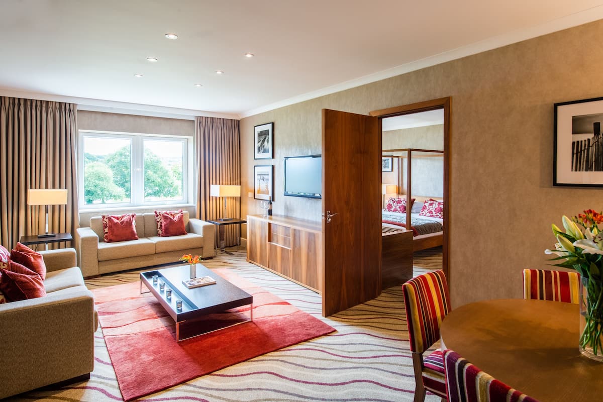 A modern hotel room with a sofa, a coffee table, a TV, and a dining area.