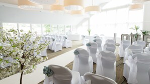 A wedding ceremony setup with white chairs, a floral arrangement, and large pendant lights. - Lakeside Park Hotel & Spa (Ryde)