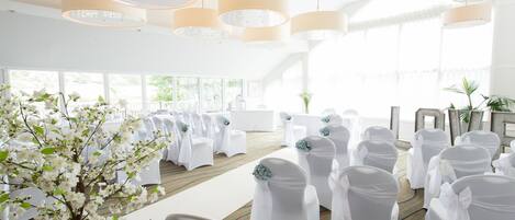 A wedding ceremony setup with white chairs, a floral arrangement, and large pendant lights.