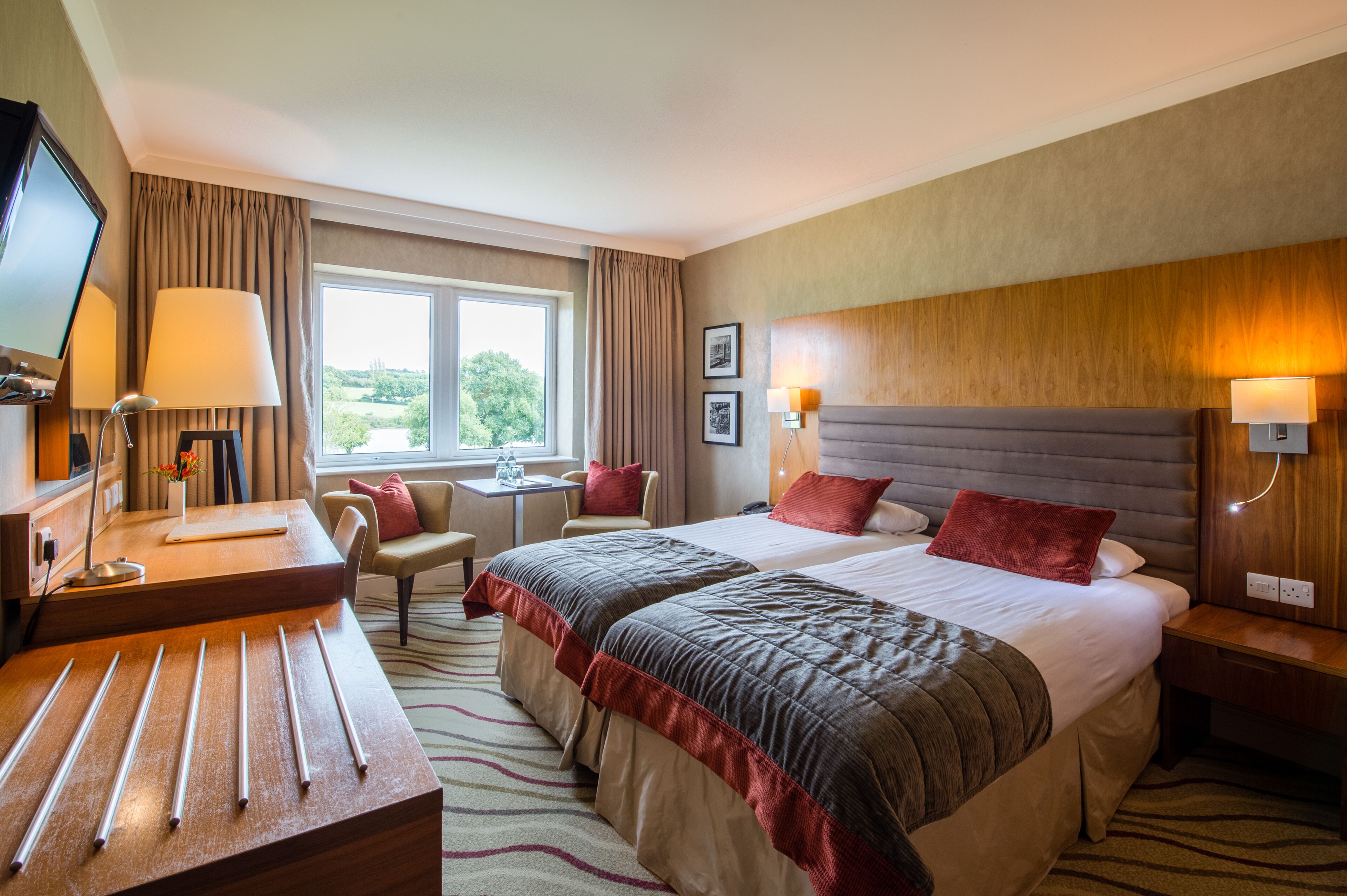 Ein Hotelzimmer mit einem großen Bett, einem Schreibtisch, einem Sessel, einem Fernseher und einem Fenster mit Vorhängen.