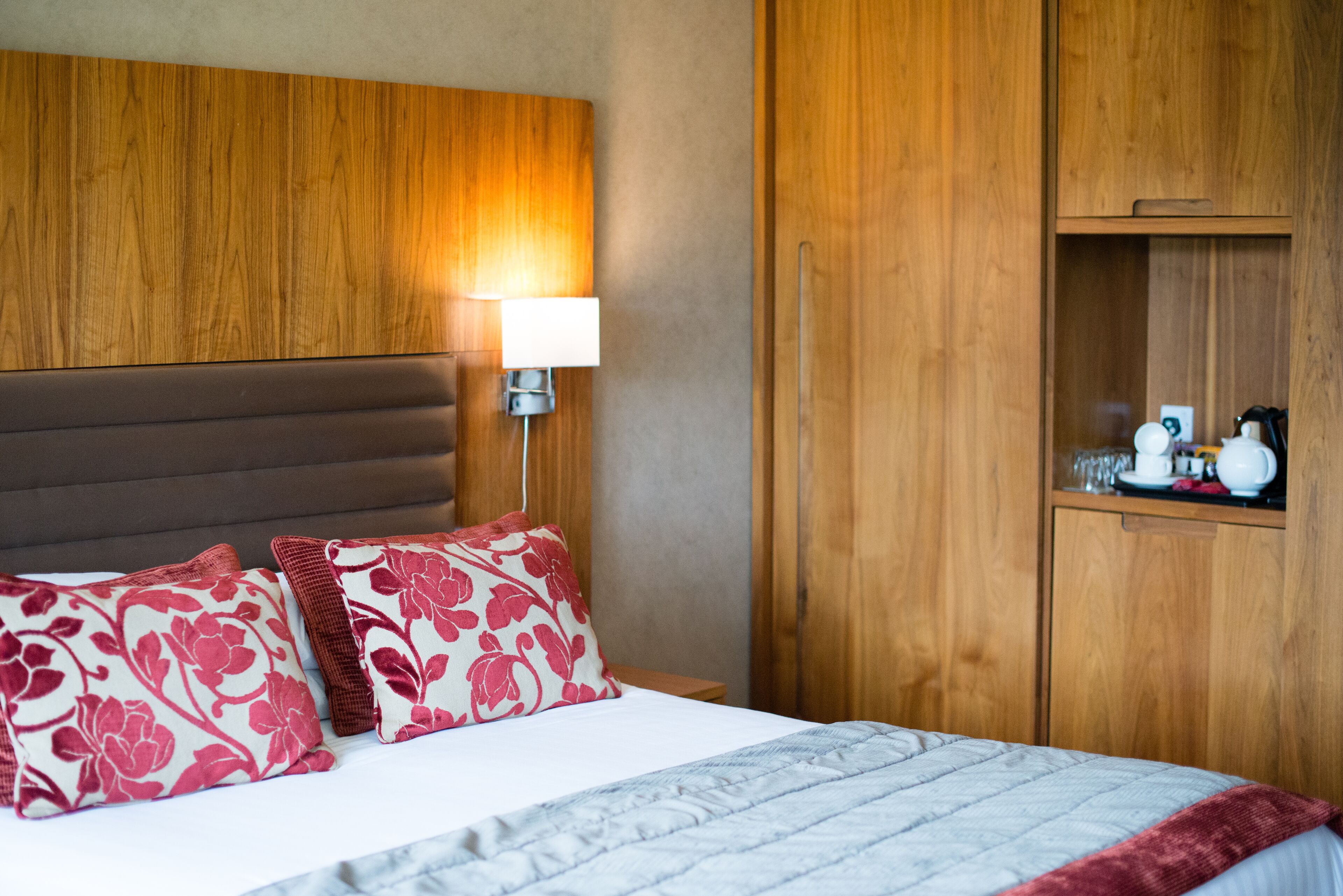 Una cama bien hecha con almohadas estampadas, una lámpara de noche y un armario de madera en una habitación de hotel.