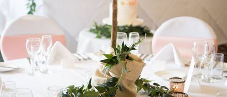 Una mesa dispuesta para una recepción de boda, con un centro de mesa floral, manteles blancos y cristalería.