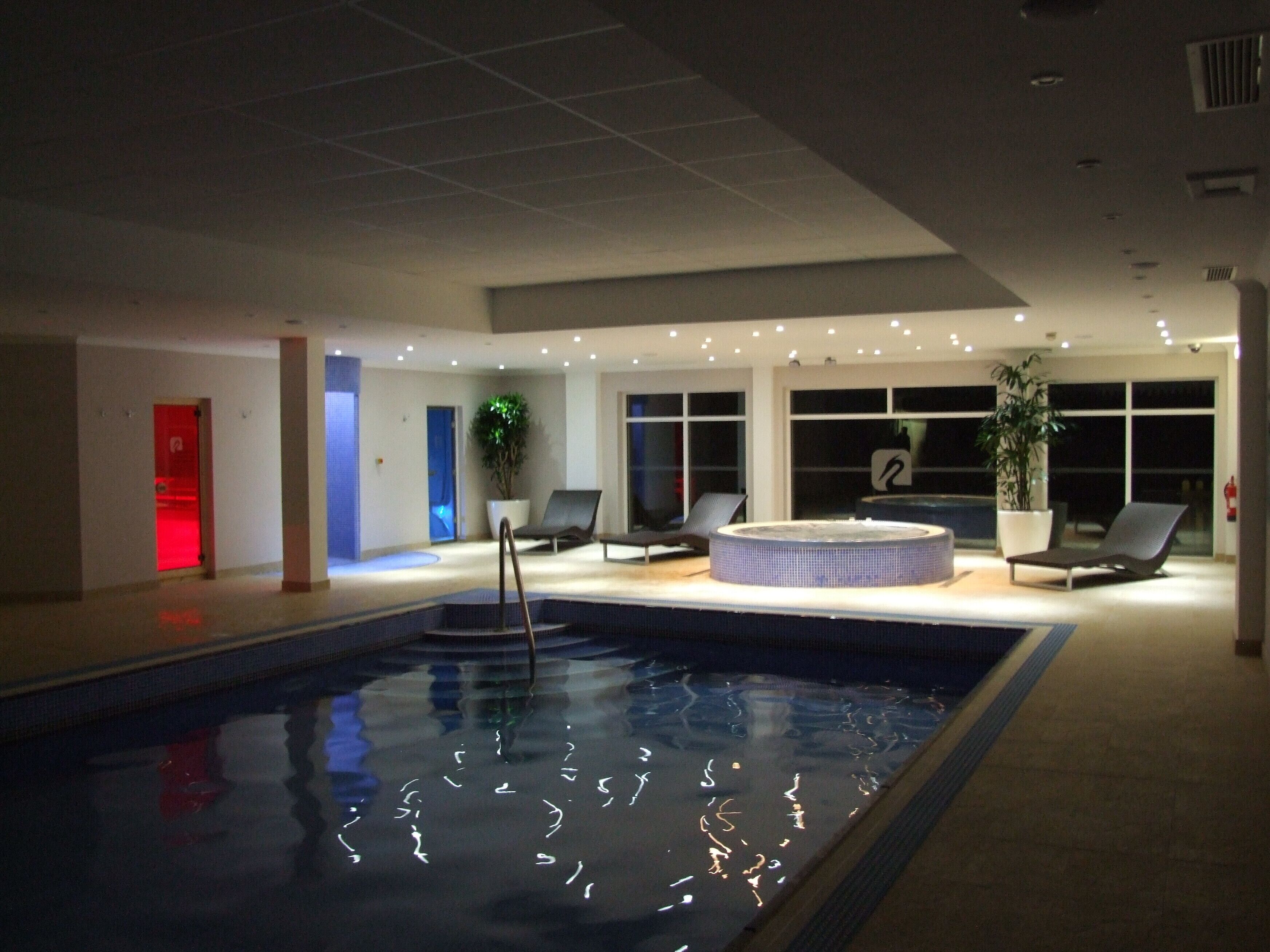 An indoor swimming pool with lounge chairs and a hot tub.