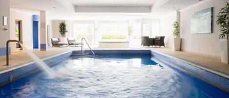 Una piscina interior moderna con agua cristalina, un trampolín y sillones de descanso.