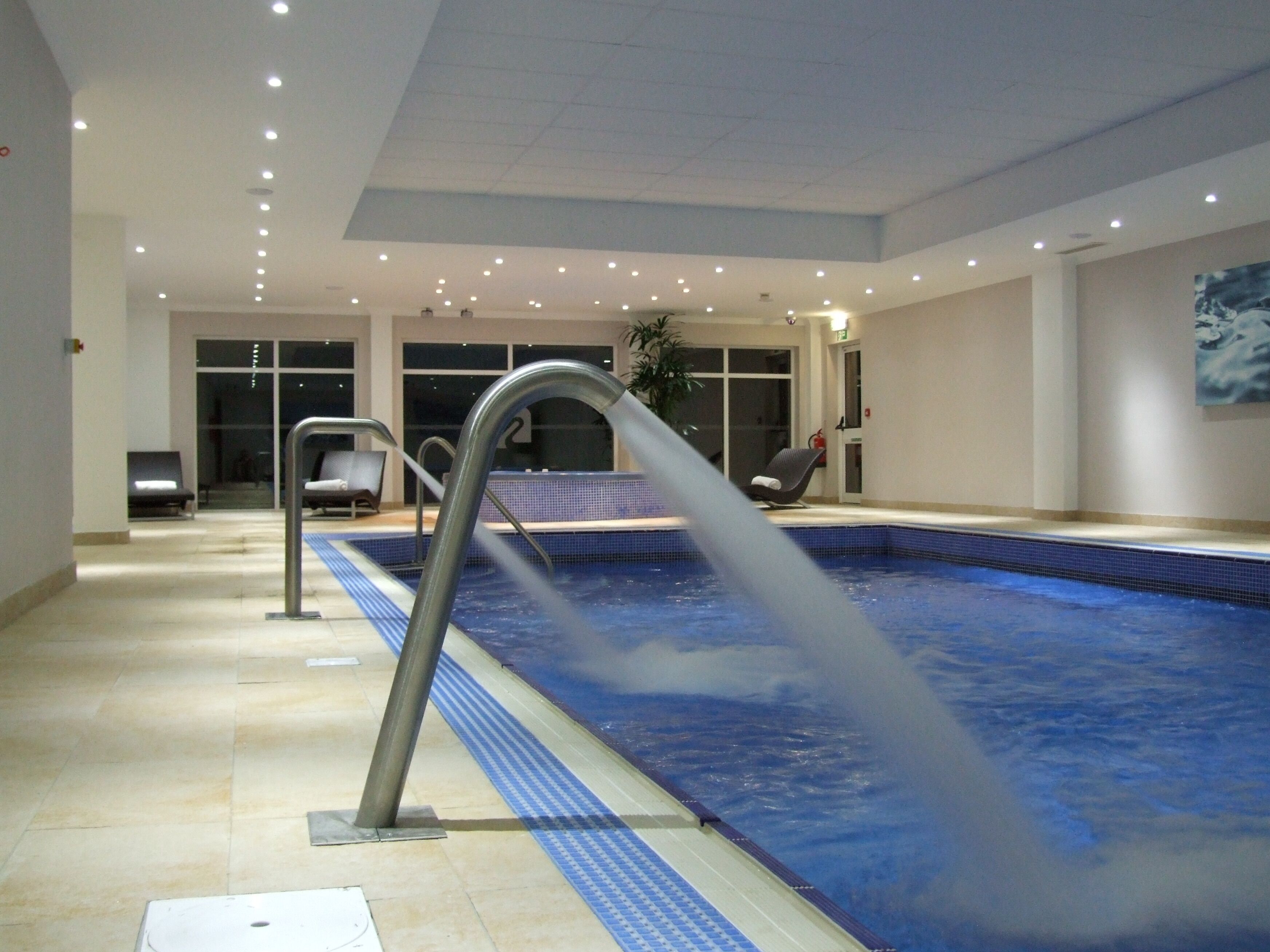 Ein Innenpool mit klarem Wasser, einer Metallhandstange und einem gefliesten Boden.