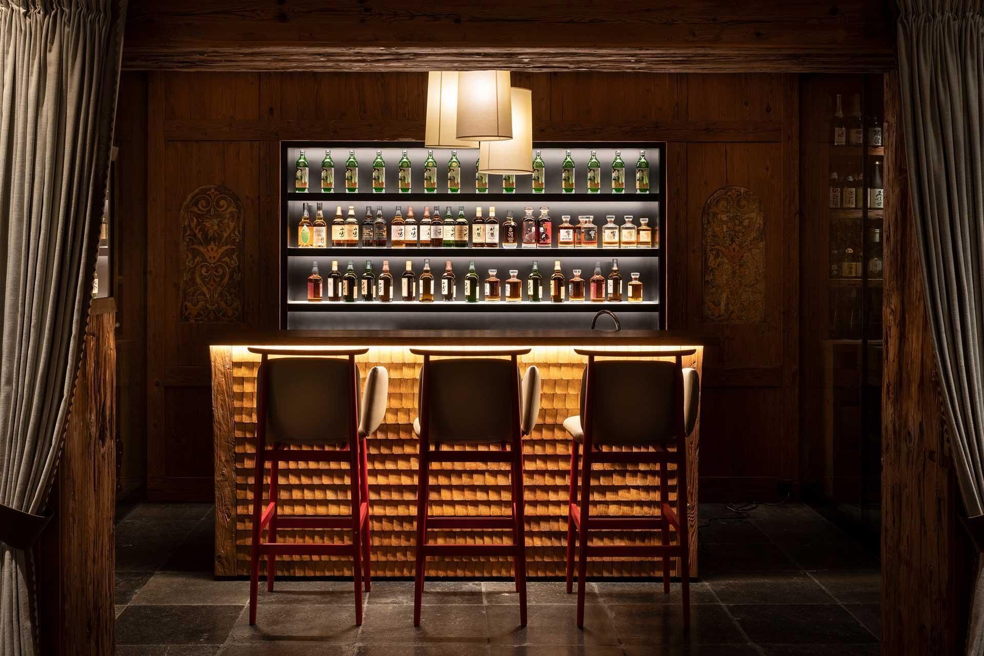 Un espace bar avec des murs en bois, une étagère remplie de bouteilles d’alcool et un comptoir avec quatre tabourets.