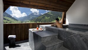 Zona de spa con vistas a montañas, techo de madera y escalones de mármol.