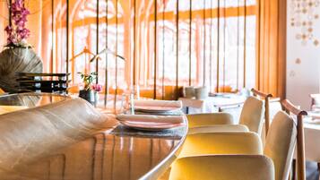 Un coin repas avec une table ronde dressée pour quatre personnes, des chaises et un vase rempli de fleurs.