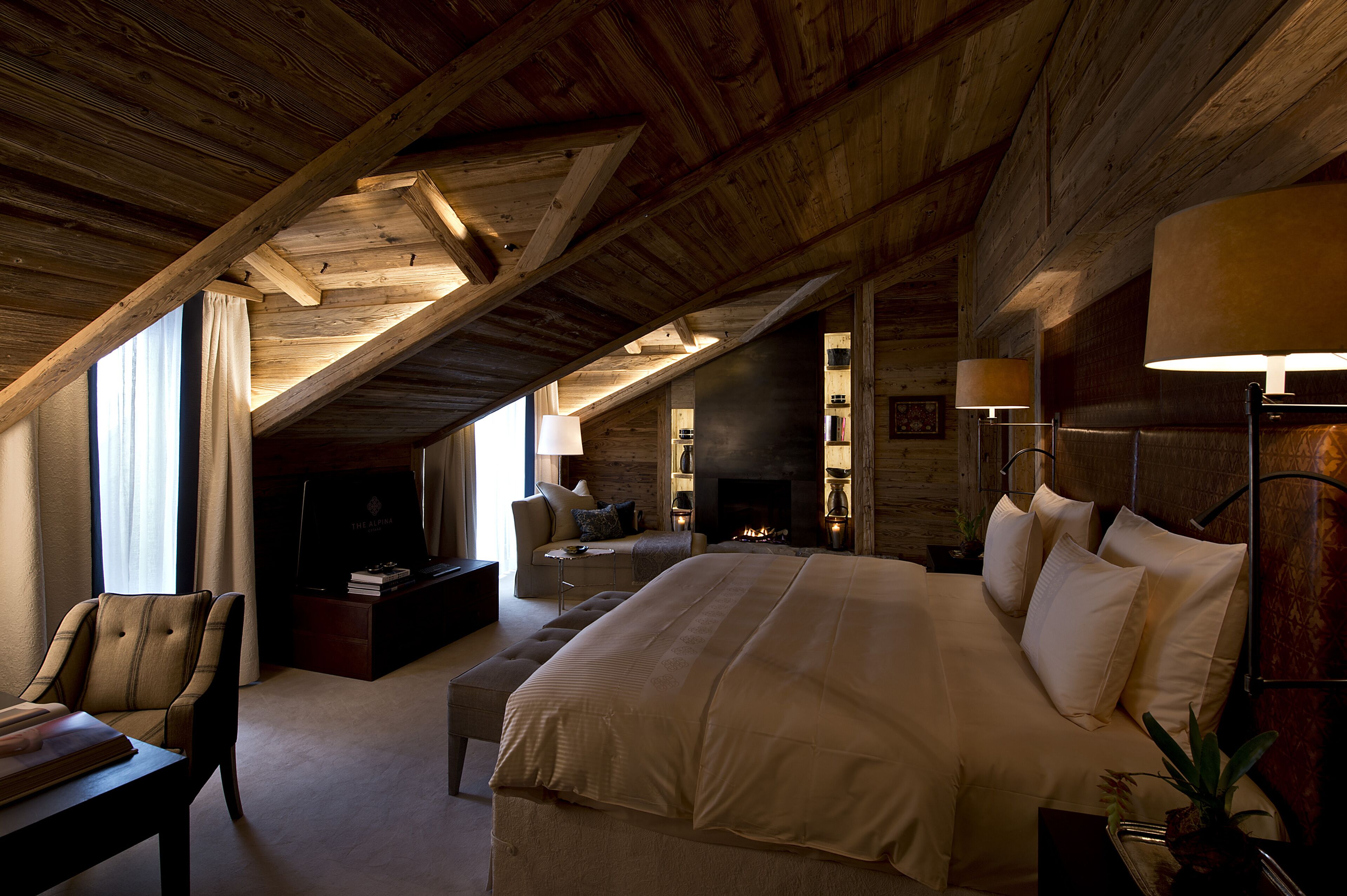 A spacious attic bedroom with a large bed, a cozy seating area, and a fireplace.