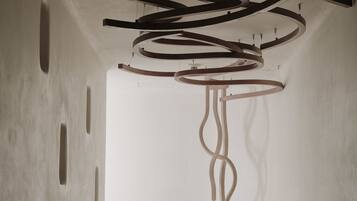 A minimalist interior with a long hallway, a large white bowl in the center, and abstract wooden ceiling structures.