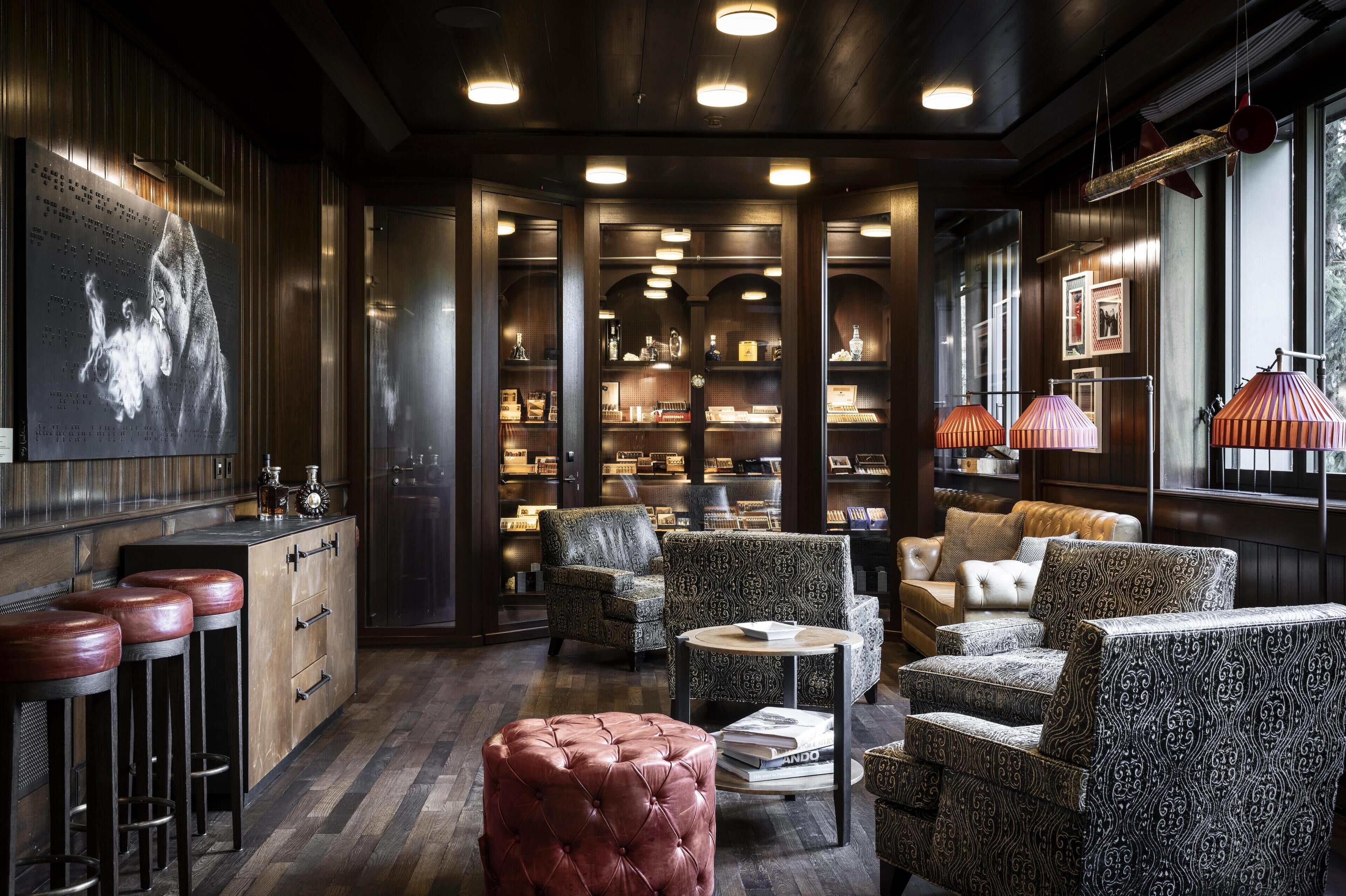 Un espace bar avec des tabourets, un pouf moelleux, des chaises à motifs et une bibliothèque remplie de bouteilles et de verres.