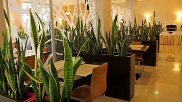 A modern hotel lobby with a seating area featuring long green plants, a decorative partition, and a buffet setup.