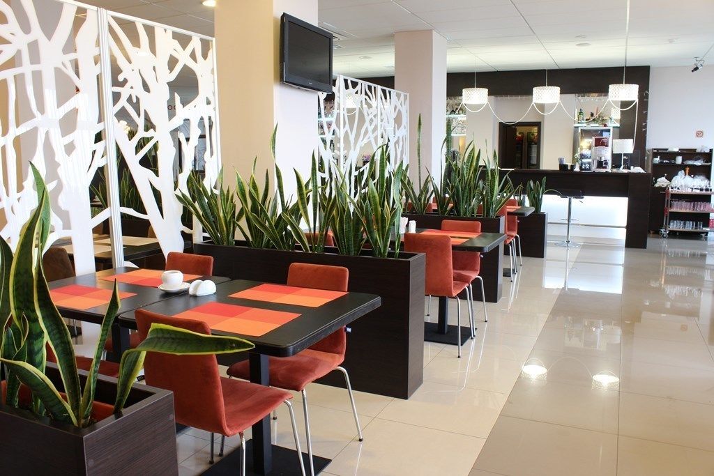 Ein modernes Restaurant mit schwarzen und roten Tischen, orangefarbenen Stühlen und Topfpflanzen.