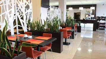 Ein modernes Restaurant mit schwarzen und roten Tischen, orangefarbenen Stühlen und Topfpflanzen.
