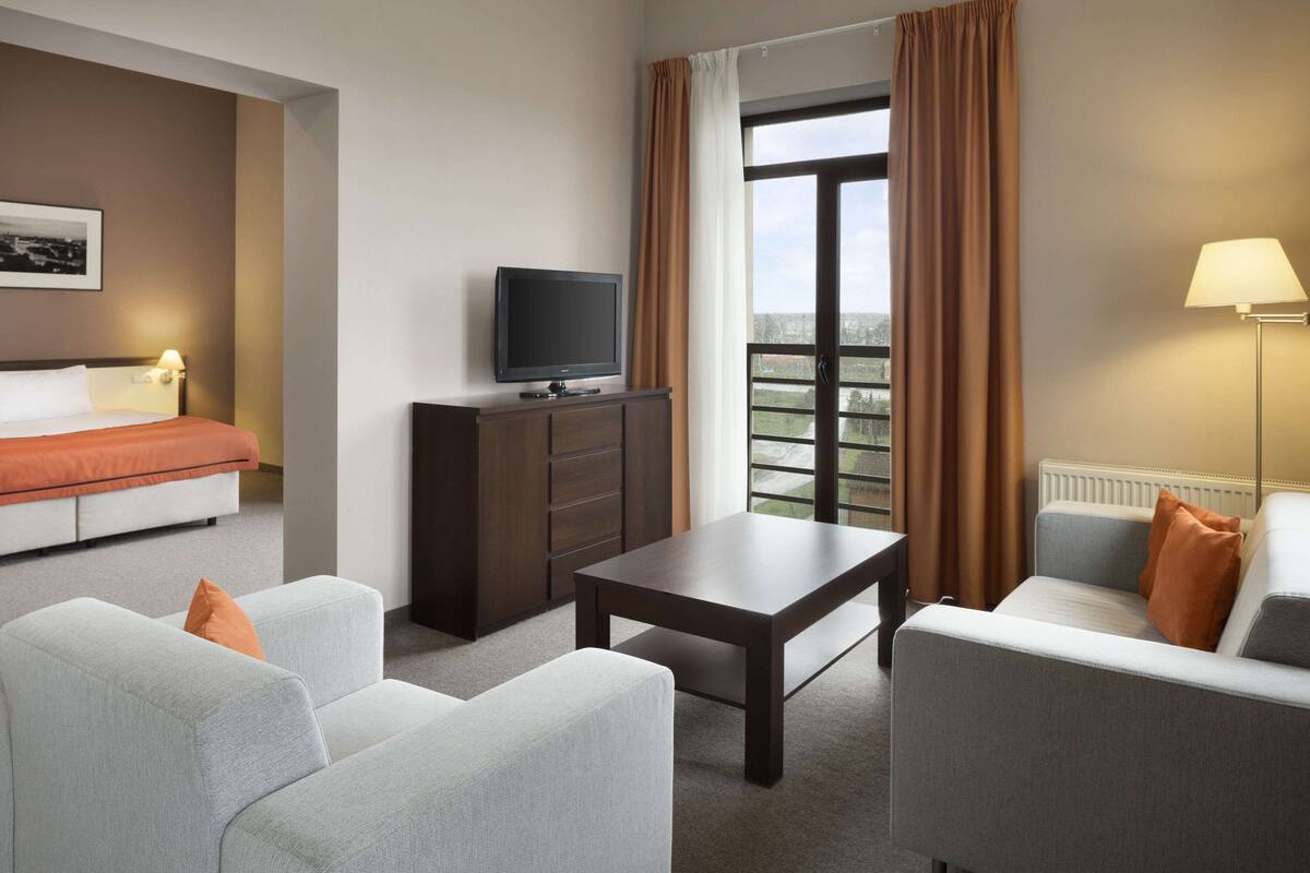 Habitación de hotel con cama, televisión en un mueble, sofá, mesa de centro y lámpara.