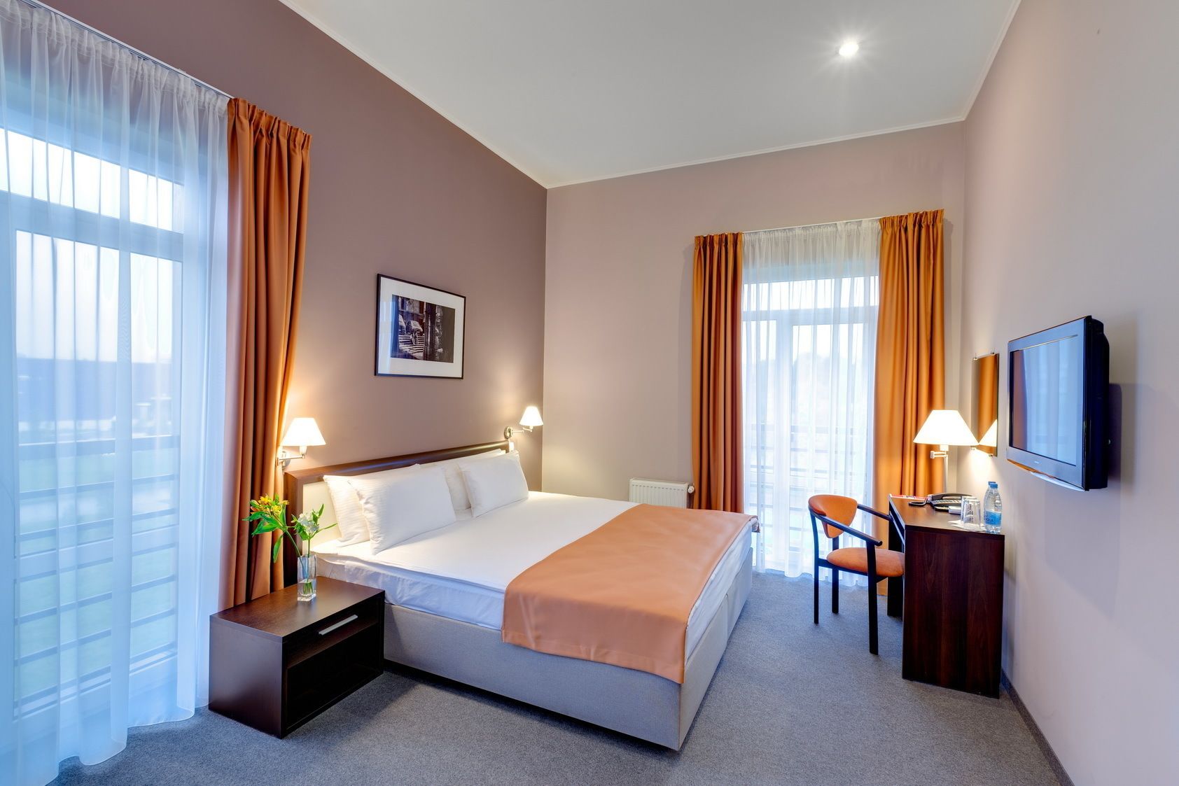 Habitación de hotel con una cama, mesitas de noche, un escritorio con silla, televisor y ventana con cortinas.