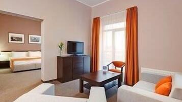 A hotel room with a bed, a desk, a TV, and two armchairs.