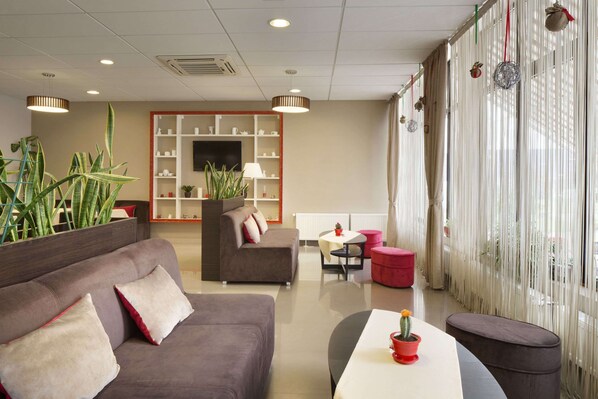 A modern hotel lobby with a sofa, armchairs, a dining area, and a TV mounted on the wall. - Ramada by Wyndham Lviv (Lviv)