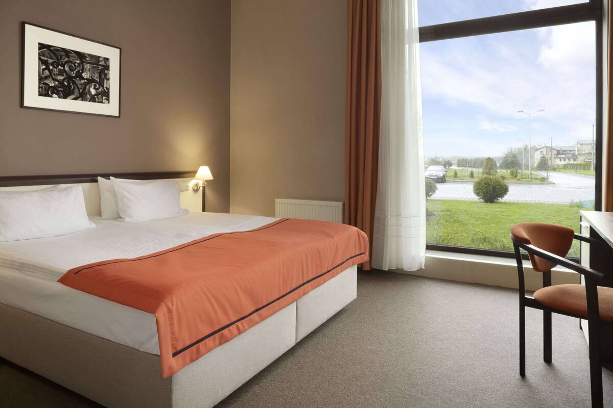 Habitación de hotel con una cama grande, un escritorio y una ventana que da a un estacionamiento y edificios.