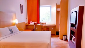 Une chambre d’hôtel comprenant un lit, un bureau avec une chaise, une télévision et une fenêtre avec des stores.