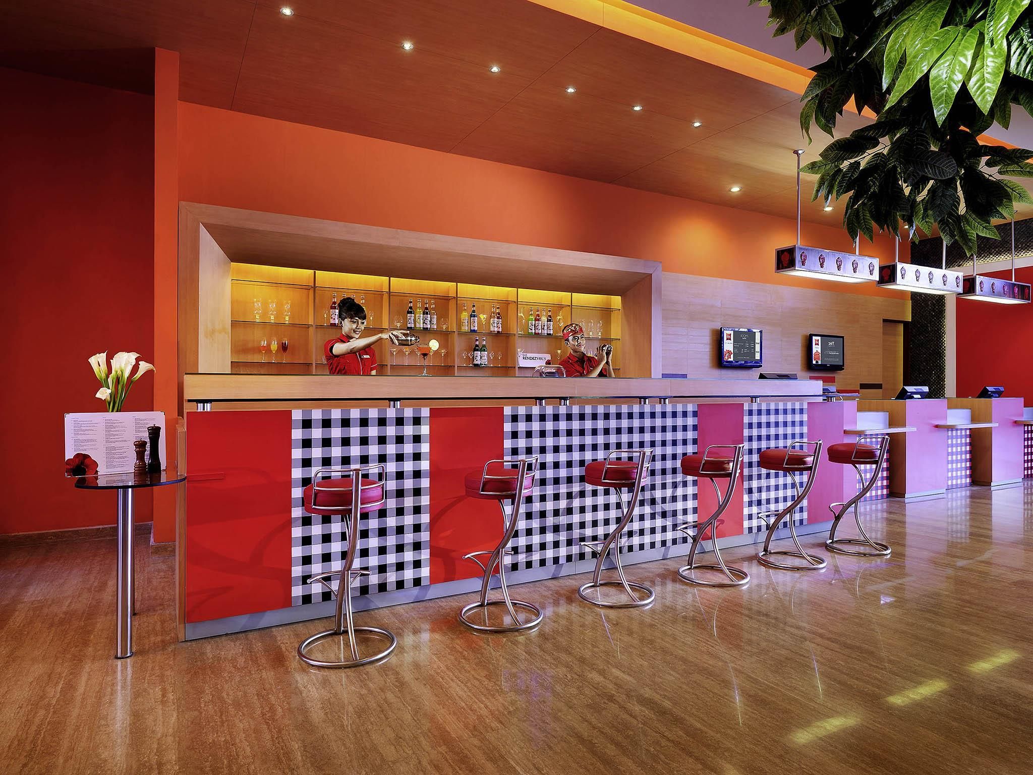 A bar area with a bartender, bar stools, and a variety of bottles and glasses on shelves.