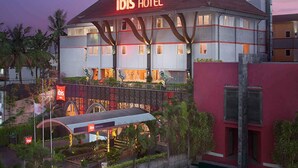 Ein Hotel mit einem gut sichtbaren 'ibis HOTEL'-Schild, einem überdachten Eingangsbereich und einer angelegten Gartenanlage.