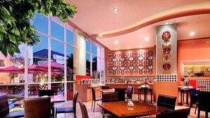 Ein Restaurant mit modernem Interieur, das einen großzügigen Speiseraum mit Tischen und Stühlen, eine Wand mit runden Tellern und große Fenster mit viel Tageslicht bietet.
