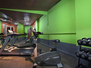 Une salle de sport équipée de tapis de course, d’un appareil elliptique et d’une série de haltères.