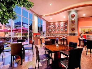 A restaurant with a modern interior, featuring a large dining area with tables and chairs, a wall decorated with circular plates, and large windows providing natural light. - ibis Bali Kuta (Tuban)