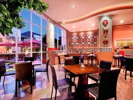 Un restaurante con una decoración moderna, que cuenta con un amplio comedor con mesas y sillas, una pared decorada con platos circulares y grandes ventanas que dejan entrar luz natural.
