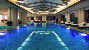 Una amplia piscina interior de diseño moderno, rodeada de sillones de descanso y un techo alto con lámparas de iluminación únicas.