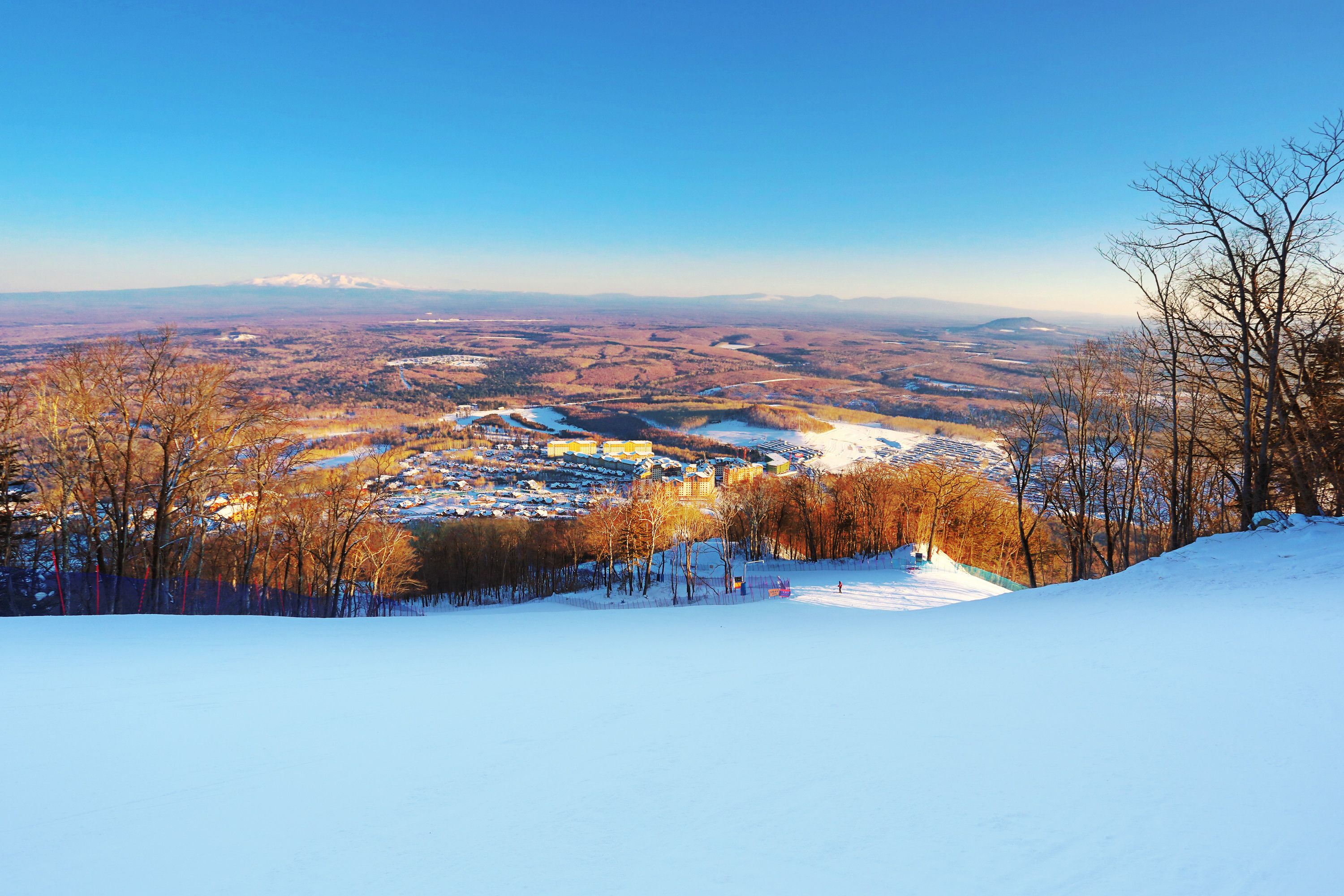 A snow-covered landscape with a view of a town and mountains in the distance.