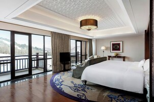 Una habitación de hotel con una cama grande, un escritorio, una silla, un televisor y un balcón con vista a las montañas.