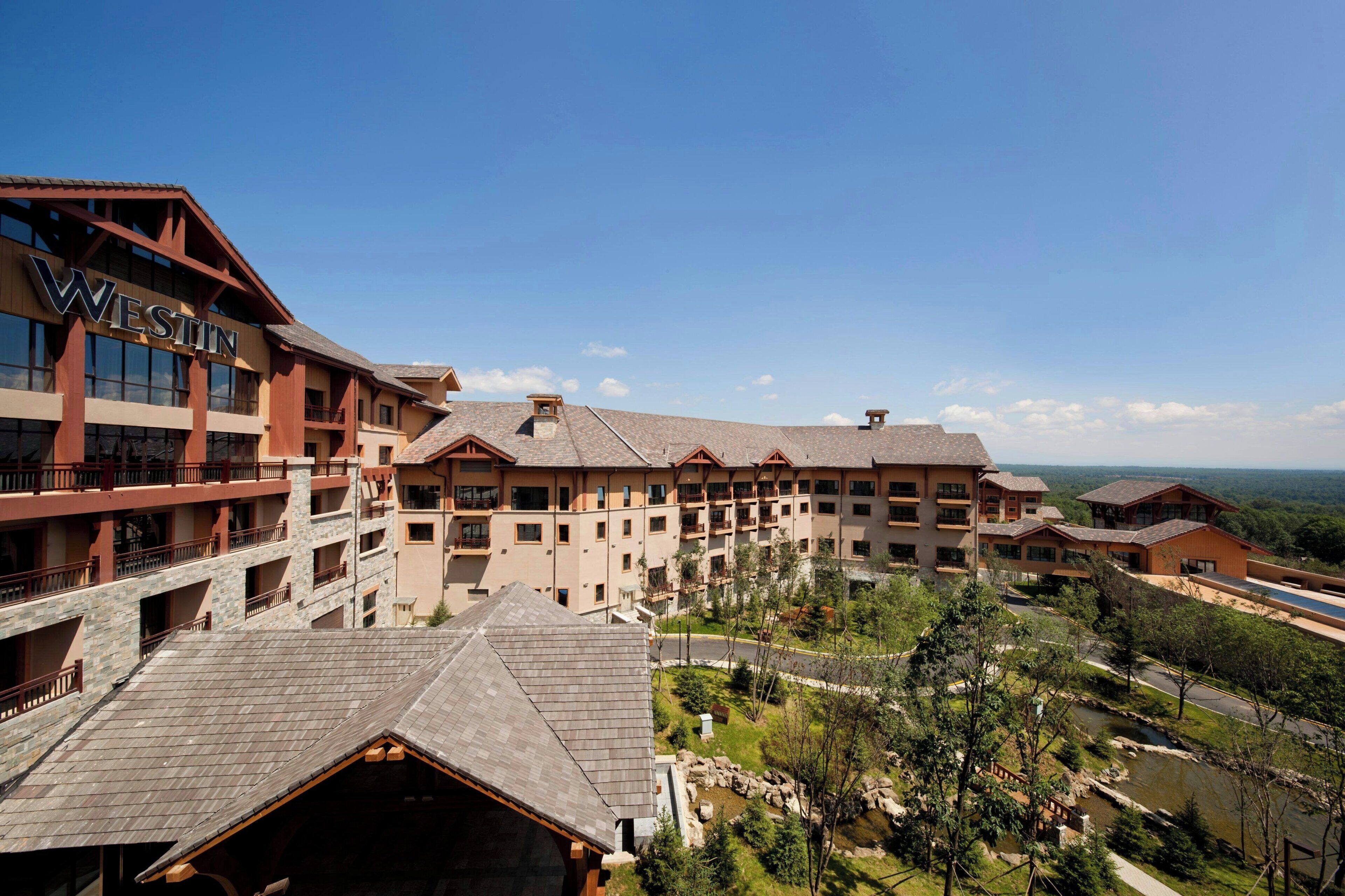 A multi-story hotel with a prominent 'WESTIN' sign, featuring a courtyard with a small pond and surrounding greenery.