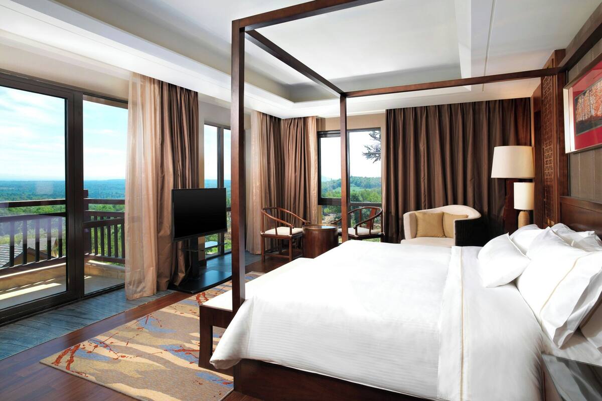 A spacious bedroom with a large bed, a television, a chair, and a view of the outdoors.