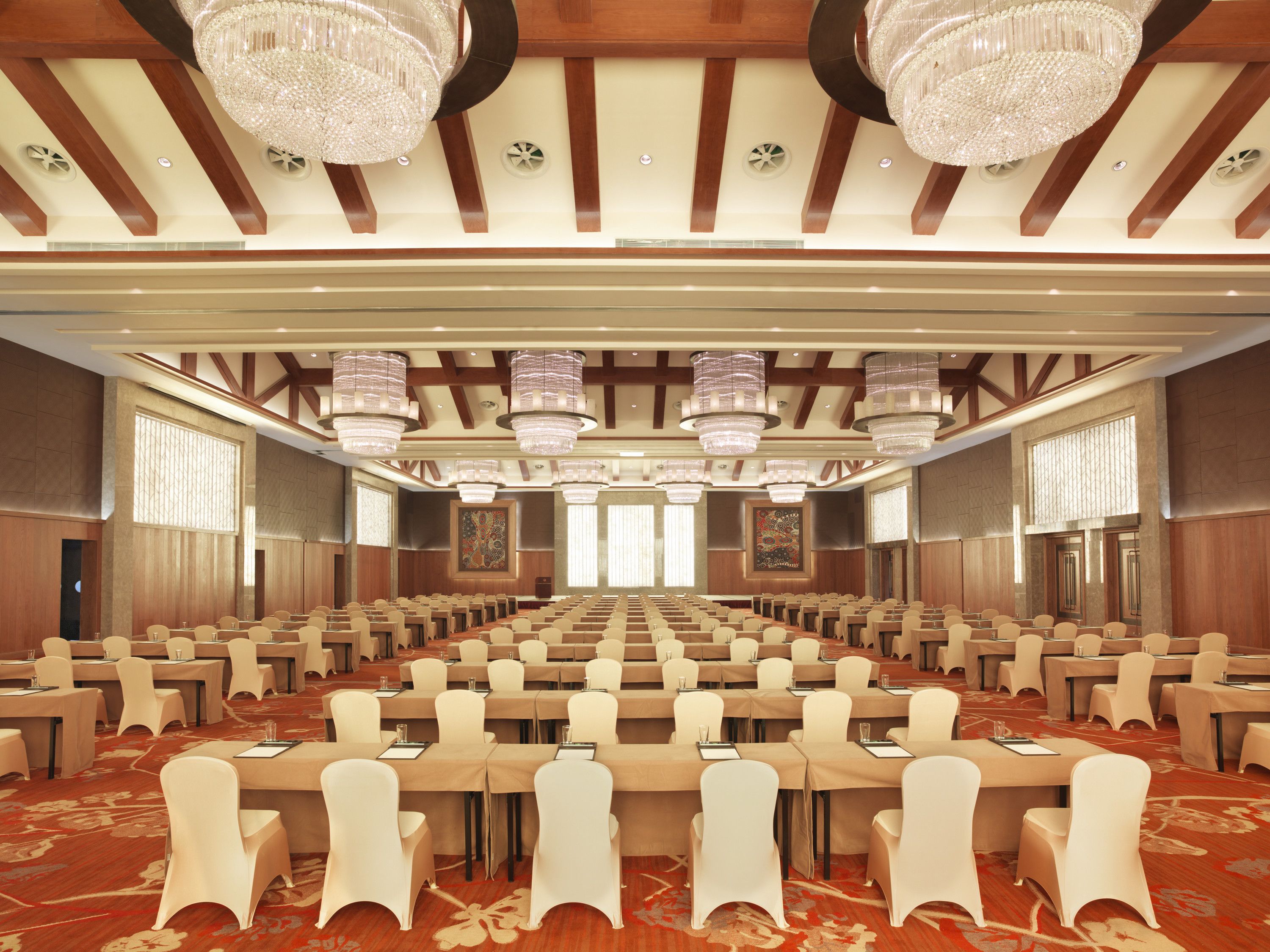 A conference room with rows of tables and chairs, large chandeliers, and wooden ceiling beams.