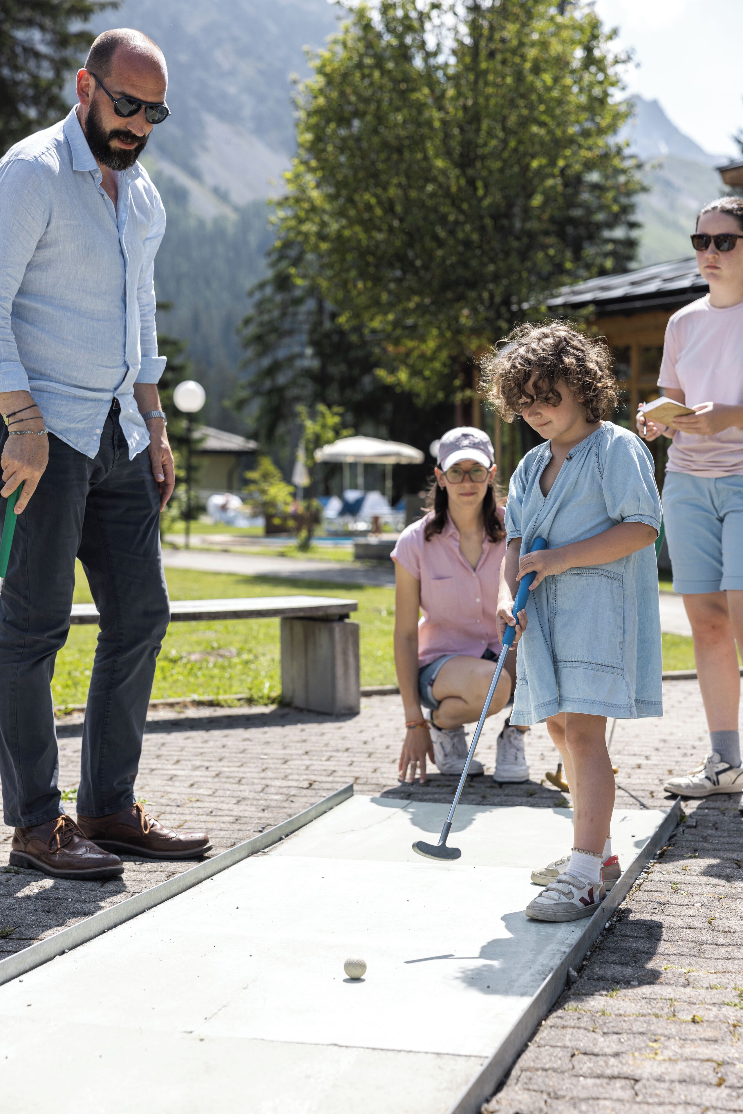 Un groupe de personnes jouant au croquet sur une surface pavée, avec une montagne en arrière-plan.