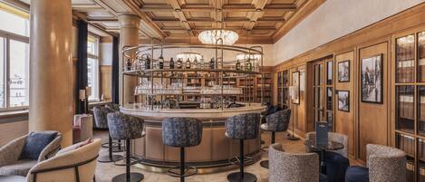 A bar area with a circular bar, multiple stools, and a chandelier.