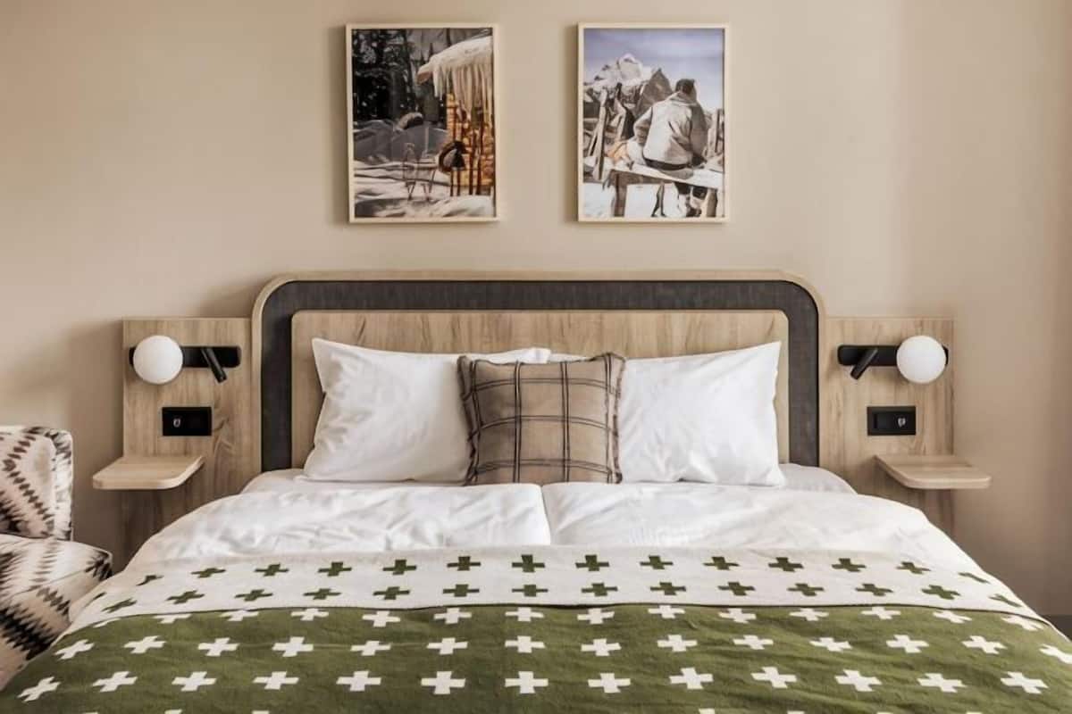 A neatly made bed with a patterned bedspread, two wall-mounted nightstands with lamps, and two framed pictures above the bed.
